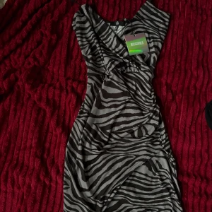 Zebramönstrad kortklänning Missguided - Säljer en snygg zebramönstrad kortklänning från Missguided. Klänningen har omlott-design och är ärmlös med coola svarta och gråa ränder. Perfekt för dig som vill sticka ut med ett djuriskt mönster och trendig passform. Har öppet jack. 💋💋