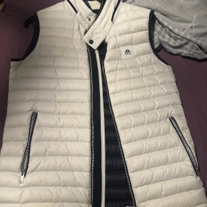 Vit och svart dunväst Moose Knuckles - Säljer en snygg dunväst från Moose Knuckles i vit och svart. Västen är äkta!!!