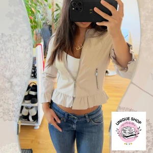 Ljusrosa croppad skinnjacka med volang - Snygg  ljusrosa skinnjacka croppad med dragkedja framtill och volangdetaljer vid nederkant och ärmslut. Jackan har lång ärm och två fickor med dragkedja. Perfekt för dig som gillar en feminin och trendig look. Passar till jeans eller kjol.