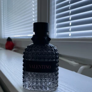 Valentino parfym med nitar - Snygg parfymflaska från Valentino med svart etikett och rosa text. Flaskan är tillverkad i glas med ett coolt nitat mönster och svart mattsvart kork med pyramidformade detaljer. Perfekt för dig som gillar lyxig och edgy design. 45ml kvar av 50ml 