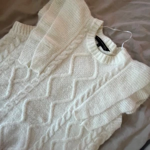 Vit stickad topp med volang - Helt oanvänd superfin vit stickad väst från Pernilla Wahlgren med breda volangärmar och snygga stickade detaljer framtill. Rund halsringning och mjukt material. Storlek Xs men passar även S