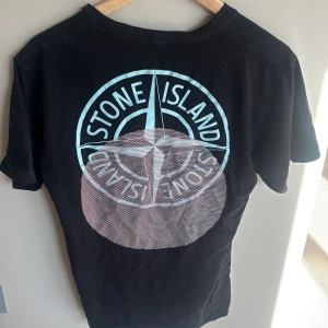 Svart Stone Island t-shirt med stor logga - Svart t-shirt från Stone Island i bomull med stor, fet logga i ljusblått och vitt på ryggen och mindre logga framtill.