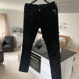 Replay svarta jeans slim fit - Svarta jeans från Replay med klassisk femficksdesign och snygga detaljer på bakfickorna. Slim fit-modell med smalare ben. Jeansen är tillverkade i stretchigt denim för skön passform och har metallknappar och dragkedja framtill.