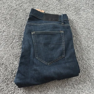 Blå jeans  Tiger of Sweden, stl 31 - Snygga blå jeans från Tiger of Sweden i klassisk straight fit med fem fickor och silverfärgad knapp. Jeansen har en mörkblå tvätt och är tillverkade i slitstark denim. Perfekta för dig som gillar stilrena och tidlösa jeans med bra passform.
