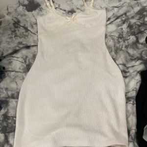 Vit ribbad spetsklänning H&M XS - Supersöt vit kortklänning från H&M Divided i ribbad bomull med spetsdetaljer och liten rosett framtill. Klänningen har smala axelband och ärmlös design, perfekt för en fräsch och feminin look. Passformen är normal och materialet är mjukt och bekvämt.