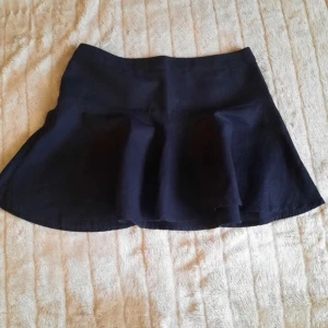 Svart kortkjol i linne, storlek 36 - Snygg svart kortkjol i linne med lätt utställd form som ger en skön och trendig siluett. Perfekt att matcha med en sommar blus eller hoodie till hösten. Kjolen har en enkel design utan mönster och passar dig som gillar stilrena plagg.