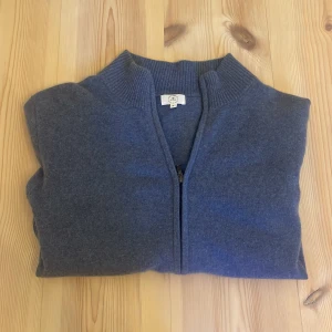 Mörkblå kofta med dragkedja - Snygg mörkblå zip tröja med hel ribbad krage. Tröjan är stickad i 100% Kashmir och har långa ärmar samt en clean, minimalistisk look. Säljs på grund av att den tyvärr blivit för liten. 