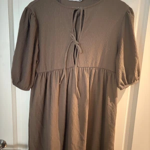 Beige kortklänning med puffärm - Supersöt beige kortklänning från 157 med puffiga kortärmar och knytning fram. Aldrig använd 