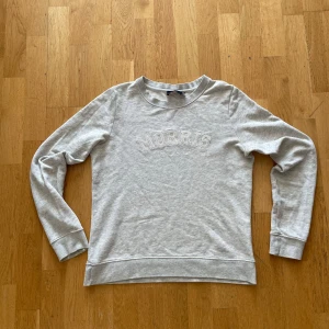 Grå sweatshirt från Morris Lady - Snygg ljusgrå sweatshirt från Morris Lady med broderad logga framtill. Klassisk rund halsringning och långa ärmar. Mjuk och skön i bomullsmix, perfekt för en chill och stilren look. Passar en som är emellan 160 till 170 cm. 