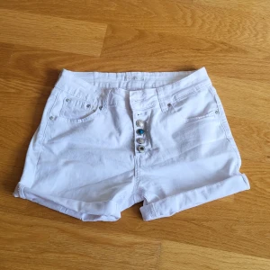 Vita jeansshorts Place du Jour - Snygga vita jeansshorts från Place du Jour. Shortsen har fem fickor, dekorativa knappar framtill och en liten stjärndetalj på bakfickan. Perfekta för varma dagar och en fräsch sommarlook.