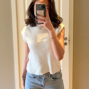 Vit ribbad ärmlös topp - Säljer en stilren vit ribbad topp från NAKD. Toppen har en rak passform och är perfekt att matcha med jeans eller kjol. Storlek xxs men sitter som en xs/s på mig som brukar bära dessa storlekar. 