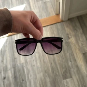 Liknar raybans boyfriend  - Stilrena solglasögon med svart båge och fyrkantig form. Glasen har en snygg lila toning som ger en cool vibe. Perfekta för att lyfta din look under soliga dagar.