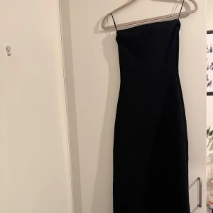 Svart axelbandslös långklänning - Säljer en svart axelbandslös långklänning och figurnära passform. Klänningen har en stilren och minimalistisk design som ger en snygg siluett. Perfekt för dig som gillar klassiska och tidlösa plagg.