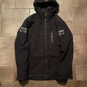 Sail Racing Vinterjacka Large - Snygg svart jacka från Sail Racing med dragkedja och huva. Perfekt för kyliga dagar med stilren design och logga på ärmarna. En av sidofickkorna har dessvärre inge dragkedja 