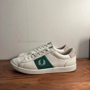 Vita Fred Perry sneakers - Säljer ett par snygga och stilrena vita sneakers från Fred Perry, original pris runt 1500kr. Skorna är i fint skick och passar perfekt nu till sommaren.