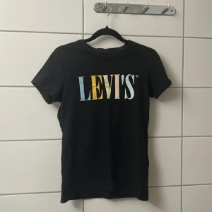 Svart Levi's t-shirt med färgglatt tryck - Snygg svart t-shirt från Levi's med stort färgglatt logotryck på bröstet i blått, gult, beige och vitt. Klassisk rund hals och korta ärmar. Perfekt till jeans eller shorts för en chill och trendig look.