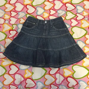 Hello Kitty jeanskjol från H&M - Mörkblå jeanskjol från H&M i storlek 128 med Hello Kitty-detaljer på knapp och bakficka. Kjolen har volangkant, fickor fram och bak samt resår i midjan för extra komfort. Perfekt för dig som gillar söta detaljer och denim. Köpt på secondhand men har endast använd en gång efter det.