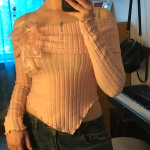 Rosa offshoulder topp  - Supersöt ljusrosa ribbad offshoulder topp från SHEIN med lång ärm och asymmetrisk nederkant. Toppen har en stor volangdetalj i organza på axeln som ger en extra girly vibe. Perfekt för dig som gillar unika detaljer och en feminin stil.