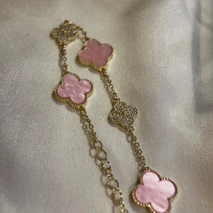 Guldarmband med rosa fyrklöver - Superfint armband i guldton med fyrklöverformade länkar. Vissa länkar är dekorerade med glittriga stenar, andra har skimrande rosa yta. Kedjan är tunn och elegant, perfekt för att ge en söt touch till din stil.