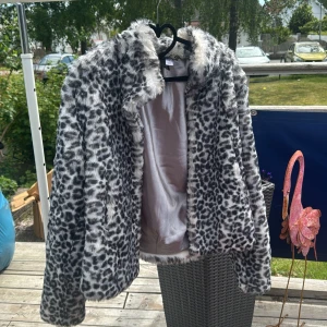 Leopardmönstrad pälsjacka stl 42 - Snygg pälsjacka i leopardmönster med svart och gråa toner. Jackan har fluffig känsla, bred krage och är helfodrad med silkeslen insida. Perfekt för dig som vill sticka ut och addera lite edge till din outfit.
