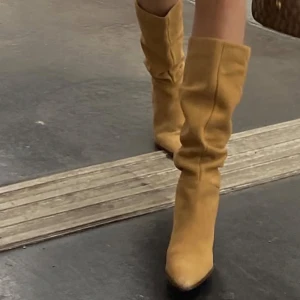 Beiga mockastövlar med klack - Snygga beiga stövlar i mocka med spetsig tå och hög klack. Stövlarna har en slouchy passform som ger en trendig look och passar perfekt till både kjol och jeans. Perfekta för höst och vinter när du vill sticka ut.