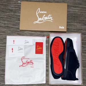 Mörkblå mocka sneakers från Louboutin - Exklusiva mörkblå sneakers från Christian Louboutin i lyxig mocka med klassisk röd sula. Skorna har rund tå, platt sula och snygga ton-i-ton snören. Perfekt för dig som vill sticka ut med stilrena detaljer och premiumkänsla.