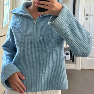 Ljusblå stickad tröja med half zip - Supermysig ljusblå stickad tröja med half zip och hög krage. Tröjan har breda ärmar och ribbad struktur. 