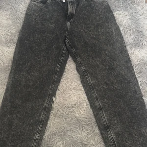 Svarta acid wash jeans från Lindex - Säljer ett par svarta acid wash jeans från Lindex med raka ben och klassisk femficksmodell. Jeansen har hög midja, dragkedja och knapp framtill. Perfekta för en cool och avslappnad stil.
