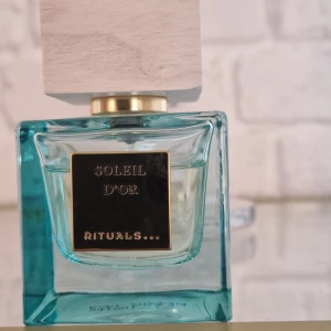 Rituals Soleil d'Or Eau de Parfum 50ml - Fräsch parfym från Rituals, Soleil d'Or, i en stilren fyrkantig glasflaska med turkos ton och stor träkork. Flaskan rymmer 50 ml och har en elegant svart etikett med gulddetaljer. Perfekt för dig som gillar exklusiva dofter och snygg design.