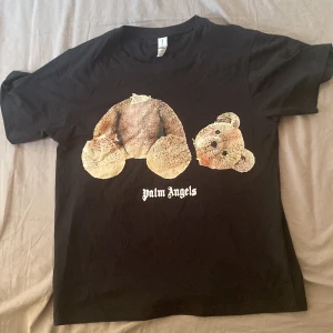 Svart Palm Angels t-shirt med björntryck - Svart t-shirt från Palm Angels med ikoniskt björntryck på bröstet och logga i vitt. Klassisk passform och rund hals. Tillverkad i mjuk bomull, perfekt för en streetwear-look.