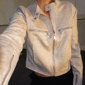 Beige mockajacka med dragkedjor - Beige mockajacka med croppad passform och silverfärgade dragkedjor på bröstet och ärmarna. Använd endast på bilderna. Nypris: 799kr 