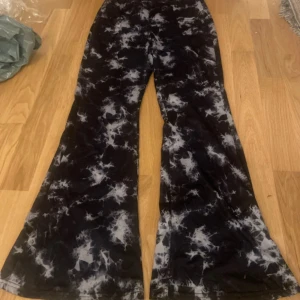 Svarta bootcut byxor från SHEIN - Bootcut byxor från SHEIN i svart och vitt tie-dye mönster. Byxorna är tillverkade i stretchigt material med 95% polyester och 5% elastan. De har en snygg utsvängd passform och normal midja, perfekta för en trendig look.