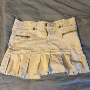 2000s jeans kjol  - Supersöt vit kort jeanskjol från Dromedar med volangkant nertill, dragkedjor framtill och broderad detalj på bakfickan. Kjolen har flera fickor, knappar och en rå kant längst ner för en vintage look.