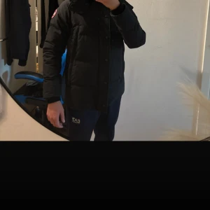 Svart dunjacka från Canada Goose - Säljer en svart dunjacka från Canada Goose med huva och snygg pälskant. Jackan har klassisk patch på ärmen, dragkedja och knappar framtill. Perfekt för kalla vinterdagar och riktigt varm. Stilsäker och tidlös modell. Jackan är äkta kvitto finns inte päls följer med 