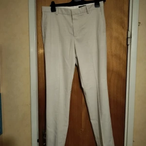 Beige kostymbyxor H&M Slim Fit - Snygga beige kostymbyxor från H&M i slim fit-modell. Byxorna har klassisk design med hällor för bälte, bakfickor dekoration och dragkedja med knapp framtill. Perfekta för en clean och stilren look. Nypris: ungefär 400kr. Pris är diskuterbart😊