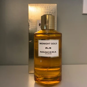 Mancera Midnight Gold Parfym - Lyxig parfym från Mancera Paris, Midnight Gold, i en stilren rund glasflaska med guldig kork. Doften har tydliga inslag av citrus, trä, kryddor, ros och amber. Flaskan är gyllene och elegant, perfekt för dig som gillar unika och fräscha doftnoter.