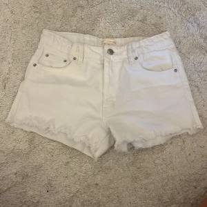 Vita jeansshorts från Gina Tricot - Snygga vita jeansshorts från Gina Tricot x Izaandelle med fransig kant nertill och klassisk femficksmodell. Shortsen har normal passform och är perfekta för varma dagar. Styla med en crop top eller hoodie för en chill look.