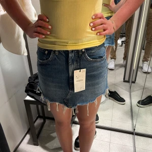 Blå jeanskjol med fransig kant - Snygg blå jeanskjol med rå, fransig kant och klassiska fickor både fram och bak. Kjolen har en kort passform och cool slitning för en avslappnad vibe. Perfekt till sneakers eller boots för en trendig look Säljer då den är för liten. Storlek S men sitter som en Xs 