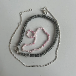 Tre halsband i silver och pärlor - Säljer tre snygga armband: ett i silverfärgad kedja, ett med svarta pärlor och ett med ljusrosa och rosa pärlor. Perfekt för att mixa och matcha till olika outfits. Alla har smidiga lås och coola detaljer.
