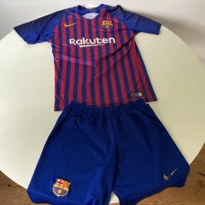 FC Barcelona Messi matchställ Nike  - Säljer ett FC Barcelona matchställ som var köpt på en marknad med Messi 10-tryck. Tröjan är blå och röd med vertikala ränder, korta ärmar och Nike-logga. Shorts är helblå med klubbmärke och Dri-FIT-material som andas. Perfekt för dig som älskar Barca och Messi!