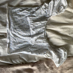 Vit blommig blus från Hollister - Supersöt vit blus från Hollister med små blå blommor. Toppen har korta puffärmar och en lätt rynkad detalj vid bysten. Perfekt för en fräsch och somrig look. Typ aldrig använt 