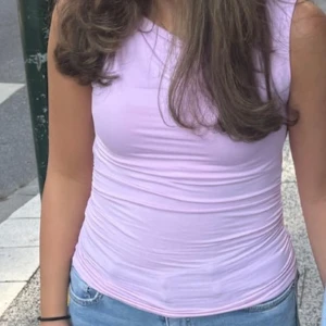 Ljusrosa topp från Gina Tricot - Supersöt ljusrosa ärmlös topp från Gina Tricot. Toppen har rynkade detaljer längs sidorna och är gjord i mjuk bomull. Perfekt för dig som gillar en enkel men trendig look.