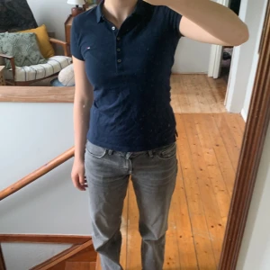 Marinblå piké från Tommy Hilfiger XXS - Snygg marinblå pikétröja från Tommy Hilfiger i slim fit-modell. Klassisk krage, korta ärmar och knappar framtill. Liten broderad logga på bröstet. Perfekt för en clean och sportig look.