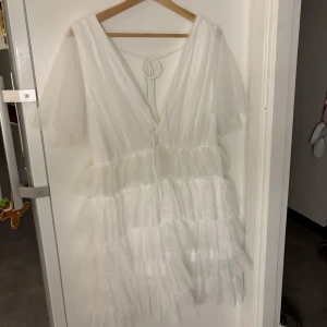 Vit volangklänning med v-ringning och öppen rygg - STUDENTKLÄNNING! Superfin vit klänning med flera lager volanger, djup v-ringning och öppen rygg med knytband. Passar perfekt nu till studenten som jag tänkte ha den till, men den var lite för stor för mig och hann inte skicka tillbaka i tid. Köpte den för 999kr och säljer för 699kr. Den är ALDRIG använd och super fin!
