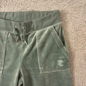 Gröna Juicy Couture byxor  - Gröna sköna Juicy couture byxor. De har två fickot fram och två stängbara fickor bak. I midjan finns ett resår som går dra åt med snörena. Köpta förra sommaren, använt ca 3 ggr sen dess. Som nya, finns inget tecken på användning❣️