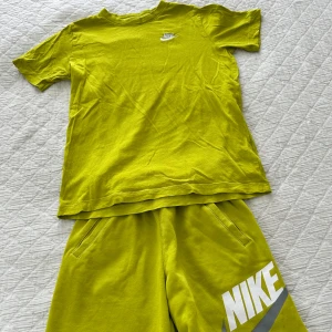 Lime shorts och T-shirt från Nike - Säljer ett par lime Nike shorts med matchande t-shirt. Shortsen har resår i midjan och två sidofickor. T-shirten har en rund hals. Perfekta för sommarens alla aktiviteter och riktigt sköna att bära.