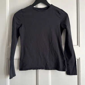 Svart långärmad tröja från H&M - En enkel svart långärmad tröja från H&M i mjuk bomull. Tröjan har rund halsringning och en rak passform, perfekt att ha som basplagg i garderoben.