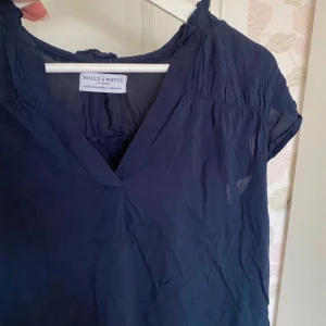 Mörkblå blus från Holly & Whyte - Säljer en mörkblå blus från Holly & Whyte by Lindex. Blusen har korta ärmar, v-ringning och är tillverkad i ett tunt, lätt material som passar perfekt till varmare dagar. Enkel och stilren design som är lätt att matcha.