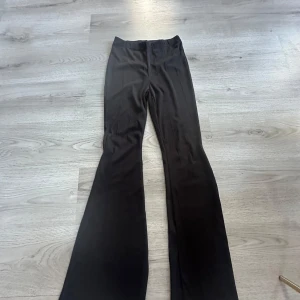 Svarta utsvängda byxor - Säljer ett par svarta utsvängda byxor med hög midja. Byxorna har en slät framsida utan synliga fickor eller detaljer och är sydda i ett stretchigt material som sitter bekvämt. Perfekta för dig som gillar en stilren och trendig look.