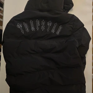 Svart pufferjacka från Trapstar - Säljer en svart pufferjacka från Trapstar. Jackan har en avtagbar huva och dragkedja framtill. Den är rejält vadderad med dun och perfekt för kalla dagar. Modellen är liten i storleken – det står XL, men den passar perfekt som en vanlig L, särskilt med en tröja under. Stilren, varm och riktigt snygg i vinter! 